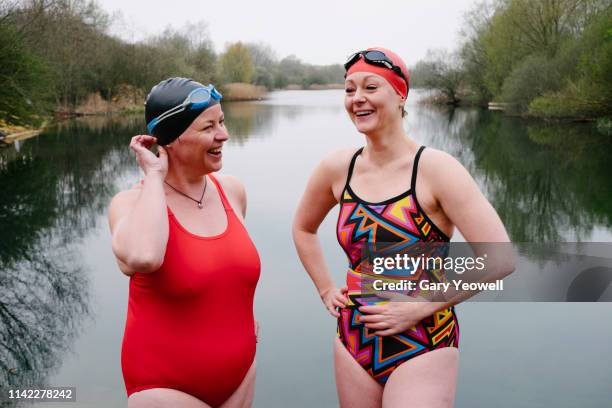 two female wild swimmers laughing by a lake - mature women swimming stock pictures, royalty-free photos & images