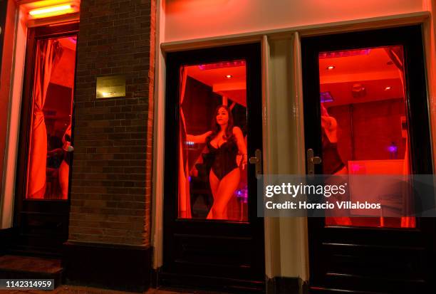 Prostitutes stand behind glass doors in the Red Light District on April 12, 2019 in Amsterdam, The Netherlands. Amsterdam is famous for its window...