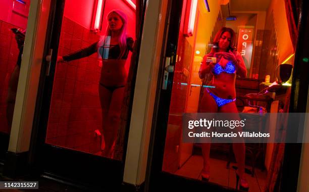 Prostitutes stand behind glass doors in the Red Light District on April 12, 2019 in Amsterdam, The Netherlands. Amsterdam is famous for its window...