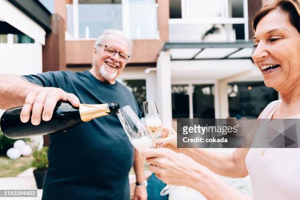 senior couple drinking champagne at home - bonding stock pictures, royalty-free photos & images