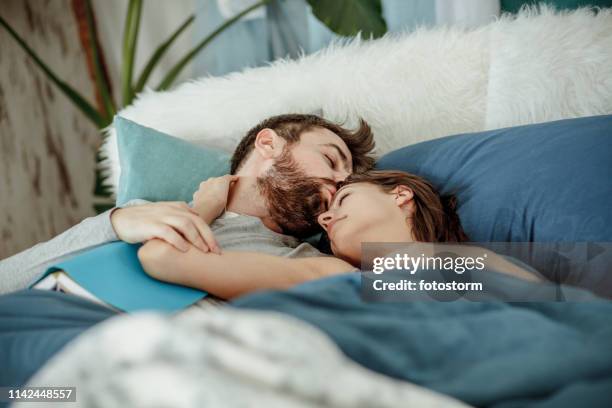 man kissing his girlfriend while lying in bed - man and woman kissing in bed stock pictures, royalty-free photos & images