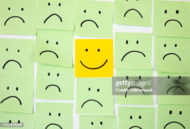 sad faces on sticky notes with one happy one - emoción negativa fotografías e imágenes de stock