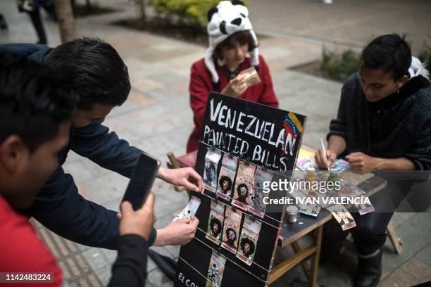 People look at Venezuelan Bolivar bills painted by Venezuelan migrants Javier Ceballos and Paula Villamizar in a street in Bogota, Colombia, on May...