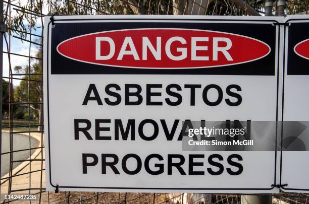 'danger: asbestos removal in progress' sign on the wire fence of a building site - asbest stockfoto's en -beelden