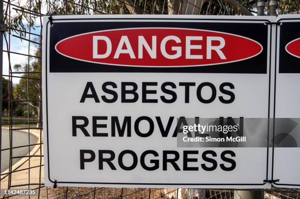'danger: asbestos removal in progress' sign on the wire fence of a building site - asbestos stock pictures, royalty-free photos & images