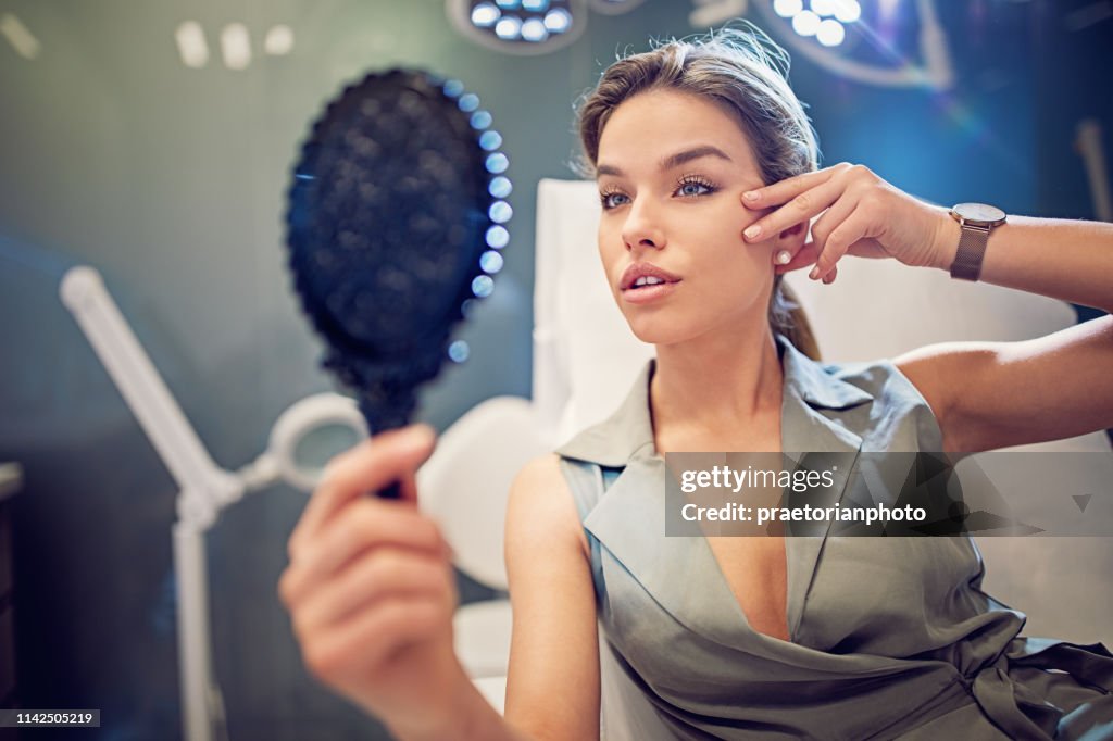 Jonge vrouw is op zoek naar haar gezicht in de spiegel na schoonheid behandeling procedure