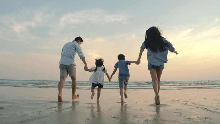 SLOW MOTION - Asian family running on the beach at sunset with happy emotion. Family, Holiday and Travel concept. Back Rear View.