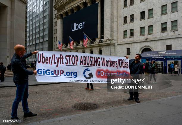 Two drivers hold up a protest sign as the Uber banner hangs on the front of the New York Stock Exchange May 10, 2019 in New York. - Uber is set for...