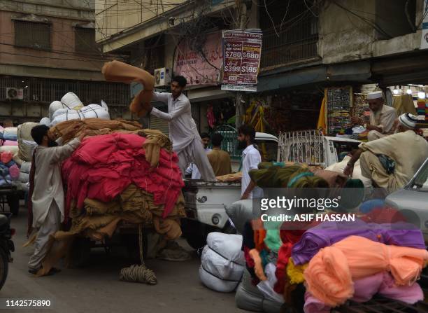 Pakistani workers load garments on a cart at a market in Karachi on May 10, 2019. - Pakistan's growth rate is set to hit an eight-year low, a...