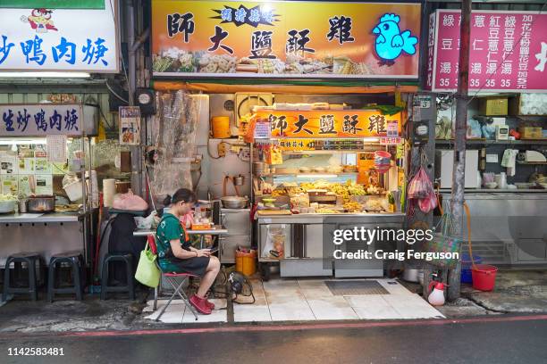 Street food vendor checks her phone while waiting for customers in the early evening at Shida night market. The lanes and alleys that make up the...