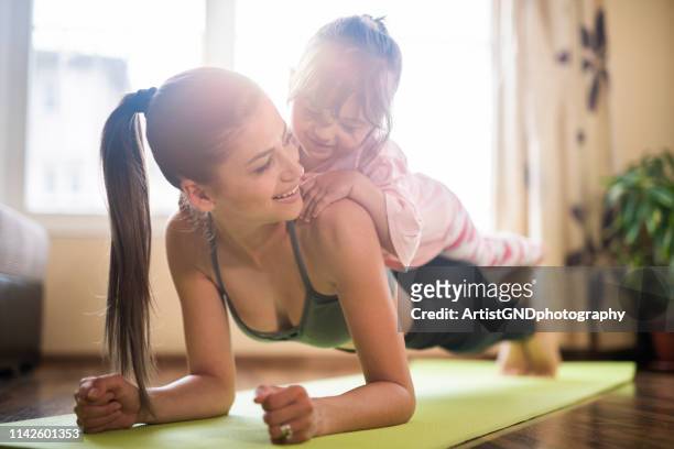 mid adult mother practicing yoga with toddler daughter on top of her, beautiful mother and daughter training home workout - family yoga stock pictures, royalty-free photos & images