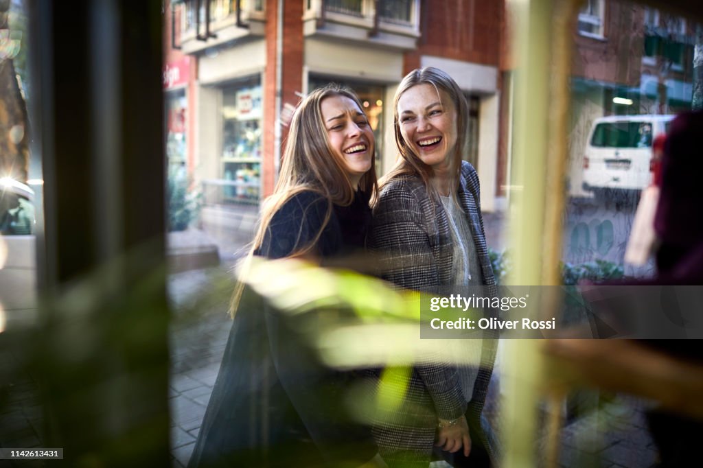 Two happy young women behind shop window