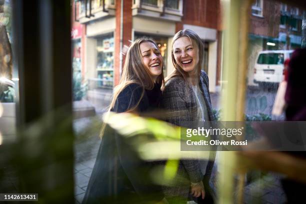 two happy young women behind shop window - buying stock-fotos und bilder
