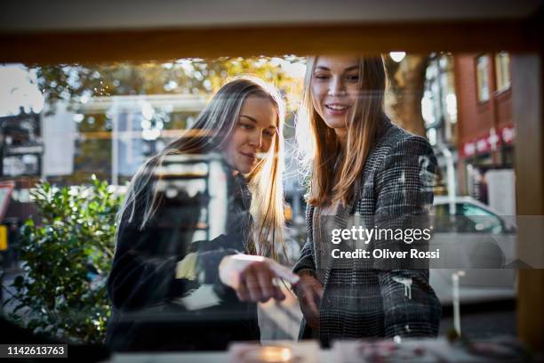 two young women looking through shop window - begehren stock-fotos und bilder