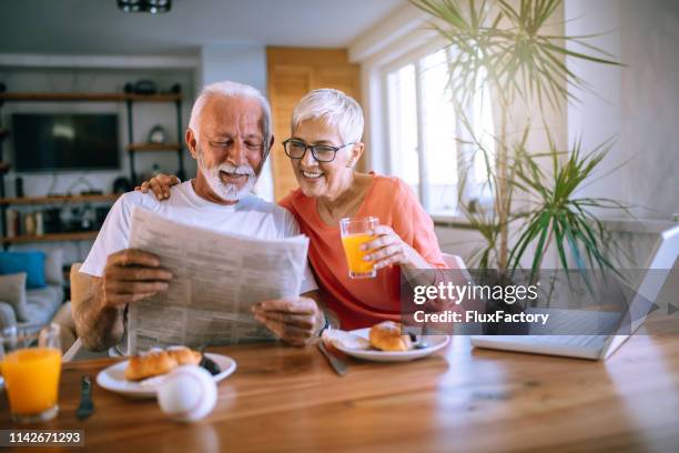 fröhliche seniorenpaare, die zeitungen lesen, während sie dessert essen - newspaper luxury stock-fotos und bilder