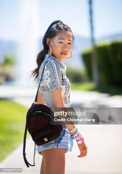 Jaime Xie is seen with festival make up wearing white cropped top, denim jeans, Chanel backpack at the Revolve Festival during Coachella Festival on...