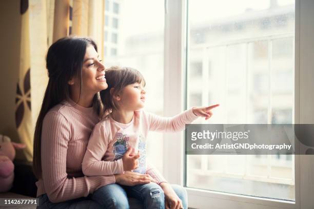 moeder en dochter samen kijken uit het raam thuis en glimlachend gelukkig. - conveyor belt point of view stockfoto's en -beelden