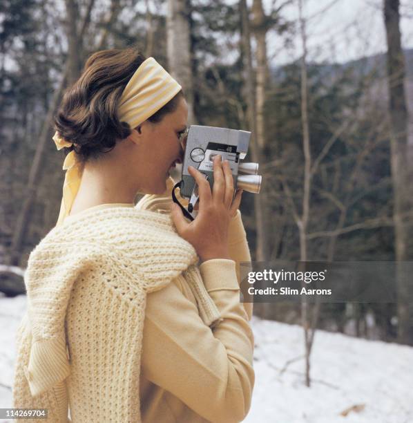 Young woman filming with a Wollensak Eyematic 8mm movie camera on the slopes of the Sugarbush Mountain ski resort in Warren, Vermont, USA, circa...