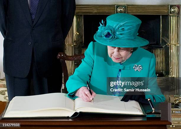 Queen Elizabeth II signs the visitors book at Aras an Uachtarain with Prince Philip, Duke of Edinburgh and Martin McAleese on May 17, 2011 in Dublin,...