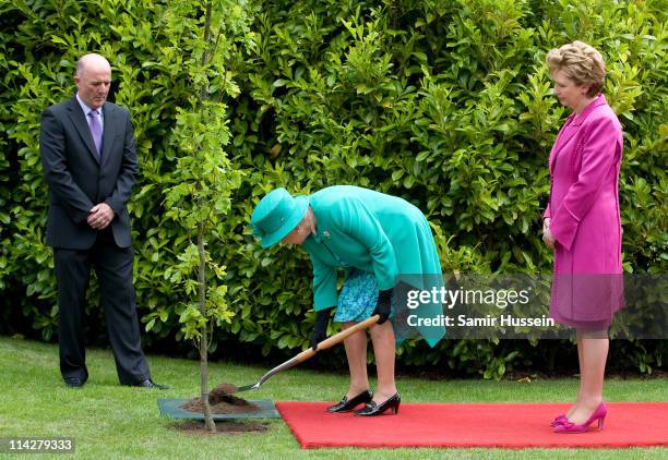 Queen Elizabeth II plants a tree as Irish President Mary McAleese looks on at Aras an Uachtarain for a tree planting ceremony on May 17, 2011 in...