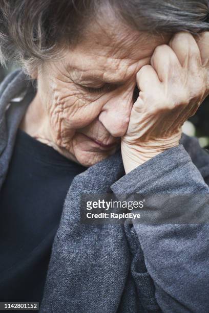 misery. a wrinkled old woman grimaces, holding her head - vulnerability stock pictures, royalty-free photos & images