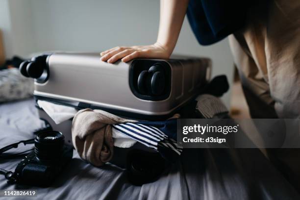 woman packing suitcase for holiday and struggling with overflowing suitcase on the bed at home - full stock-fotos und bilder