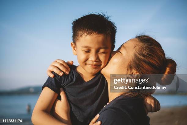 mother kissing her son's cheek - kota kinabalu beach stock pictures, royalty-free photos & images