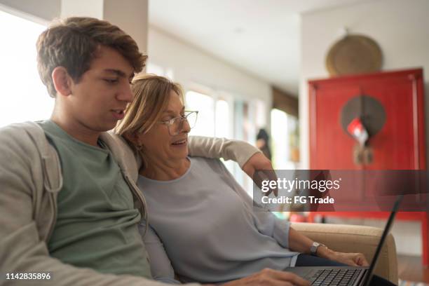 teenager junge und reife frau mit laptop, während auf dem sofa im wohnzimmer sitzen - grandmas living room stock-fotos und bilder