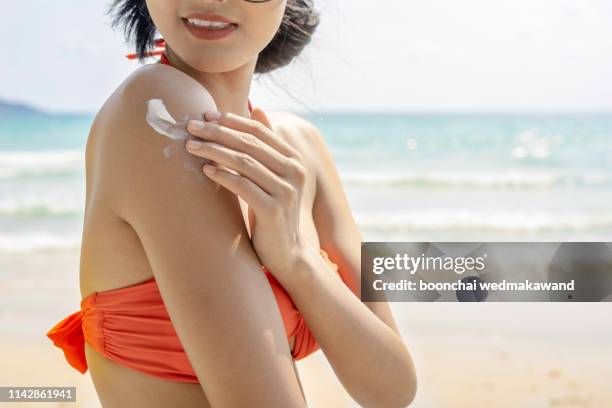 young woman with sun shape on the shoulder holding sun cream bottle on the beach - suntan lotion stock-fotos und bilder