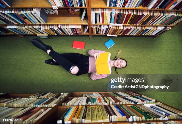 jeune étudiant se trouvant sur le plancher dans la bibliothèque et le livre de lecture. - bookshelf photos et images de collection