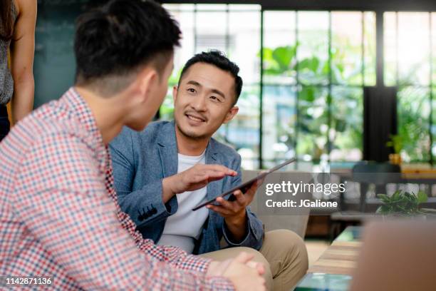 medewerkers die een informele bijeenkomst in een modern kantoor - business chinese men talking stockfoto's en -beelden