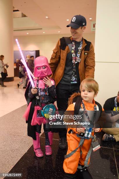 Portrait of a man as he escorts two children, one dressed as a pink version of 'Darth Vader' and the other as a 'Rebel Pilot,' at the Star Wars...