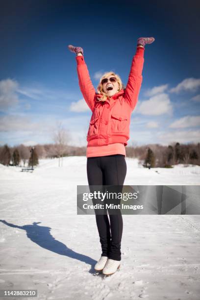 caucasian woman on ice skates cheering on frozen lake - blonde cheering stock-fotos und bilder