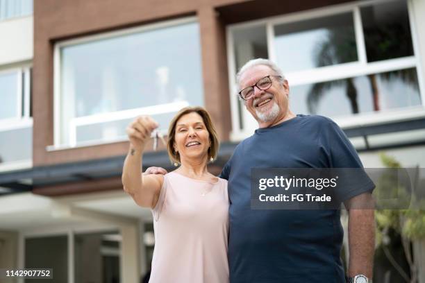 mature couple holding the keys from their new house - senior moving house stock pictures, royalty-free photos & images