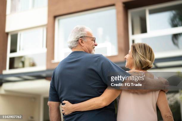 rear view of mature couple in front of a house - senior moving house stock pictures, royalty-free photos & images