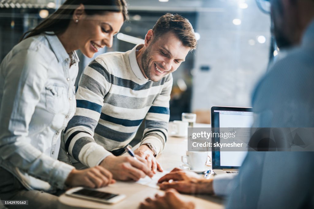 Pareja feliz firmando un contrato en una reunión de negocios con su agente de seguros.