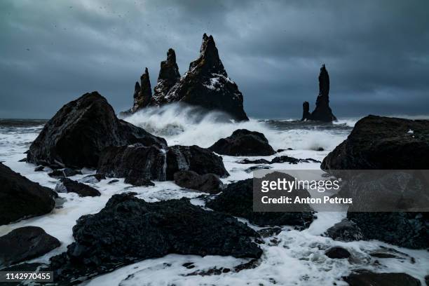 basalt rocks troll toes on black beach. at storm reynisdrangar, vik, iceland. - basalt stockfoto's en -beelden