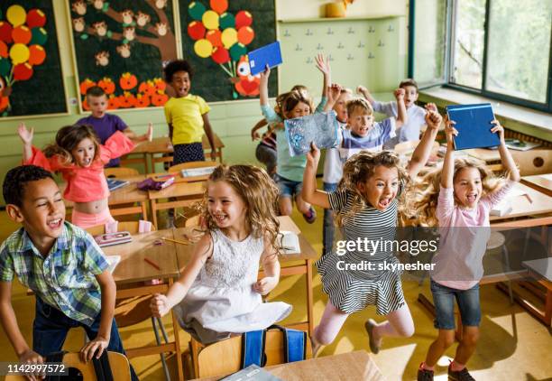 large group of joyful elementary students jumping in the classroom. - finale celebration stock pictures, royalty-free photos & images