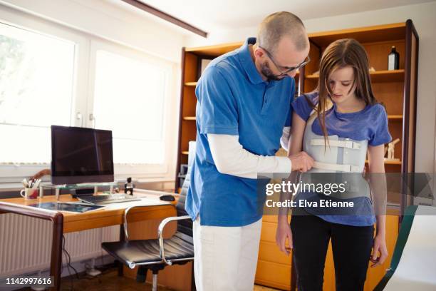 male gp in a german medical office, assessing teenage girl wearing back brace for scoliosis correction - skolios bildbanksfoton och bilder