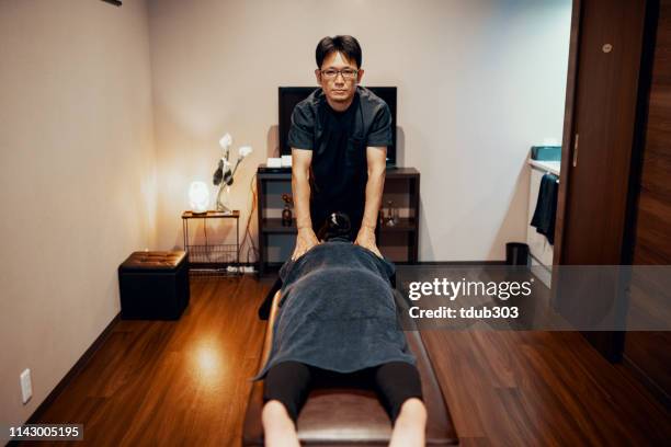 mid adult woman having her shoulders and back massaged at a health spa - massage table stock pictures, royalty-free photos & images