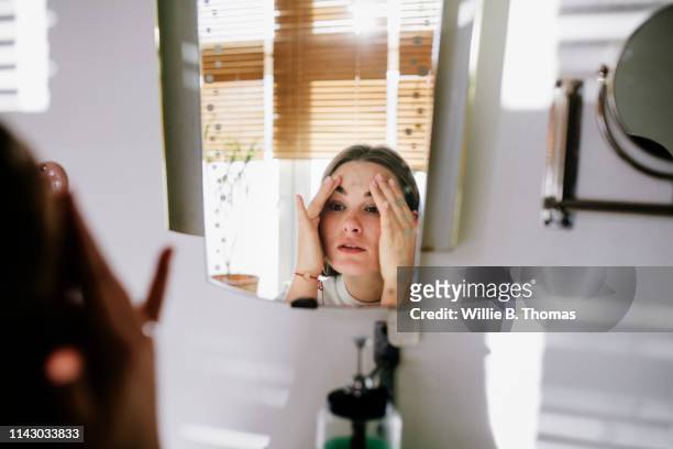 woman looking in bathroom mirror - sehen stock-fotos und bilder