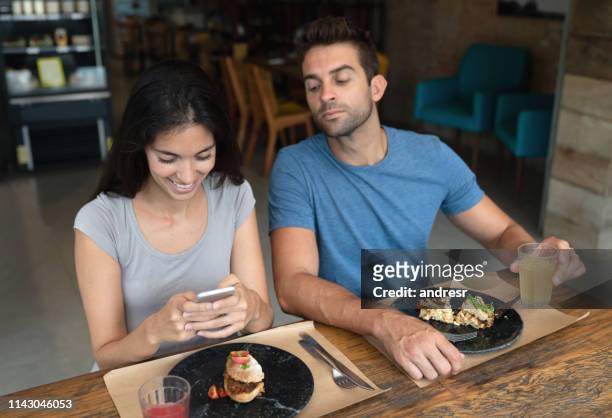 woman texting at a restaurant and boyfriend trying to see her phone - covet stock pictures, royalty-free photos & images