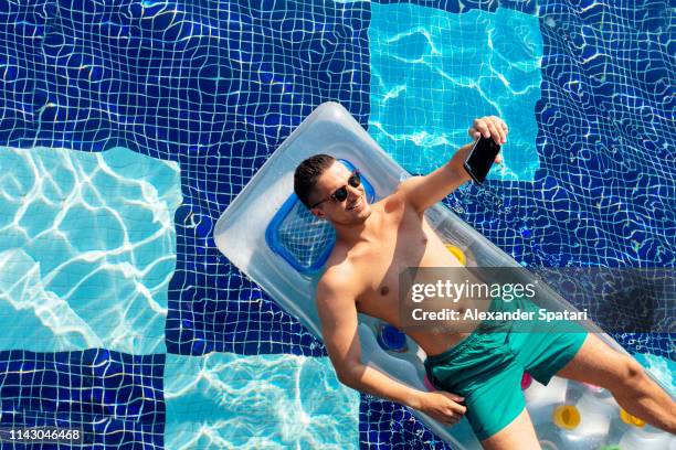 smiling man in sunglasses on inflatable pool raft taking selfie with smart phone - man in swimming pool stockfoto's en -beelden