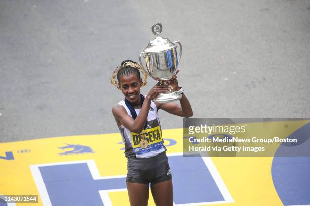 April 15, 2019: Women's winner Worknesh Degefa hoists up the trophy at the finish line of the 123rd Boston Marathon on Monday, April 15, 2019 in...