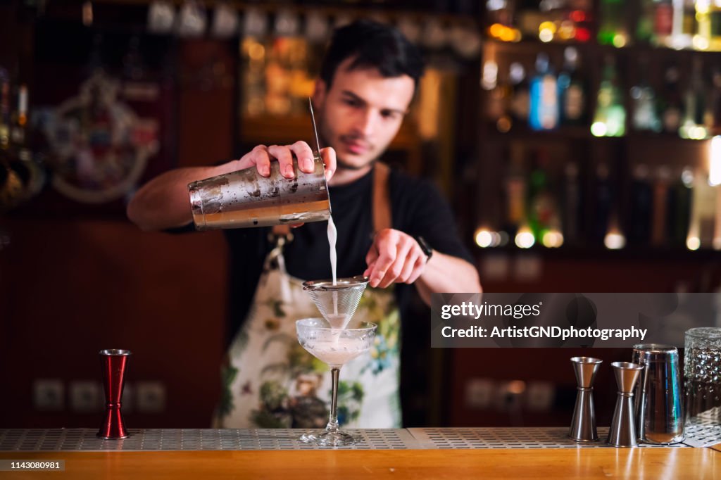 Barman masculino que derrama o álcool no vidro, um bartender novo que faz o cocktail luxuoso.