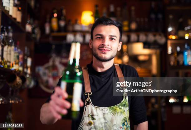 smiling caucasian bartender serving beer at bar - beer bottle stock pictures, royalty-free photos & images
