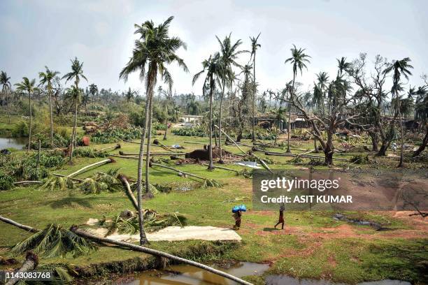 This picture taken on May 10, 2019 shows people walking next to pulled up trees in Puri in the eastern Indian state of Odisha after the passage of...