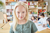 Lovely albino girl smiling and looking at camera while standing on blurred background of classroom in art school