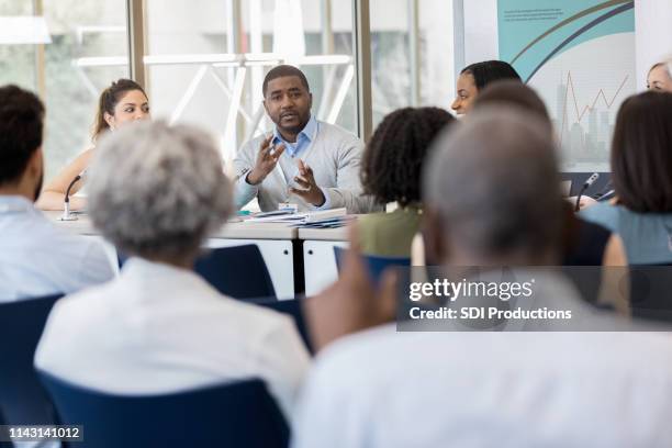 mid adult man répond aux questions - table ronde réunion photos et images de collection