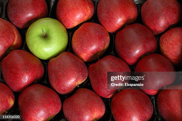 one green apple among the reds - duality stock pictures, royalty-free photos & images